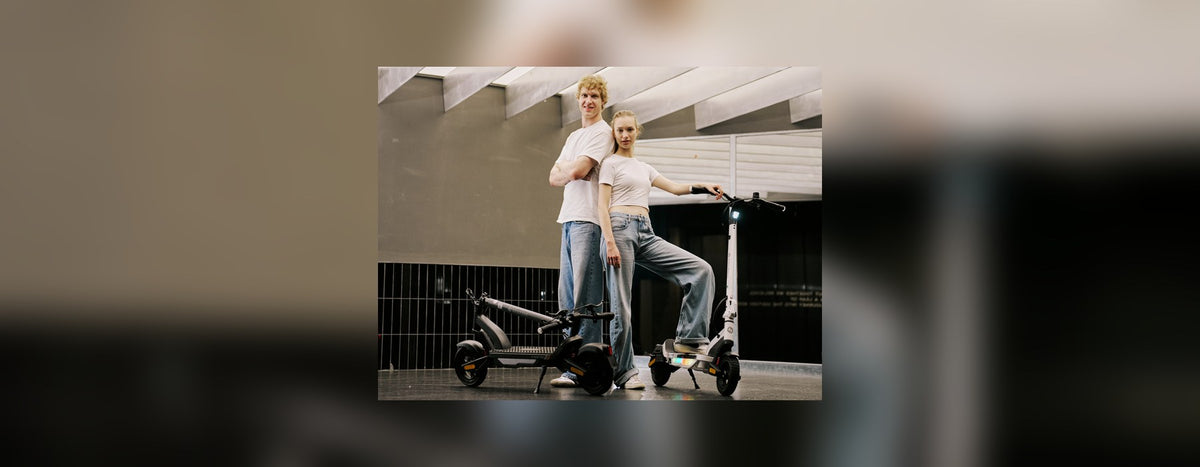 Two people standing with black and white isinwheel electric scooters beside a railing outdoors