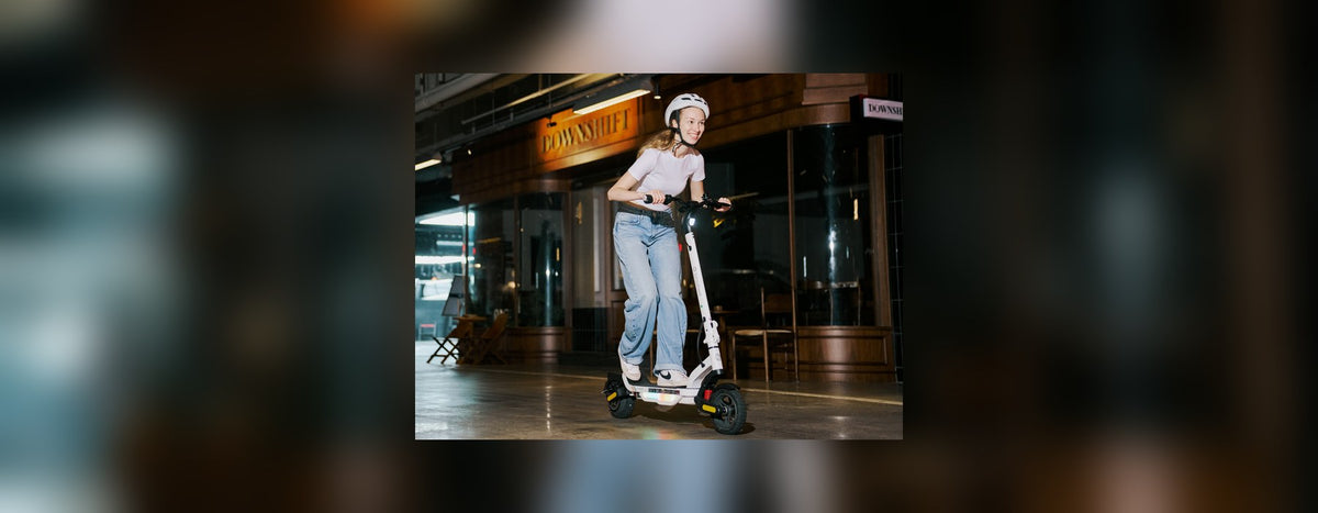 Woman in a helmet riding a white isinwheel electric scooter along a city street at night