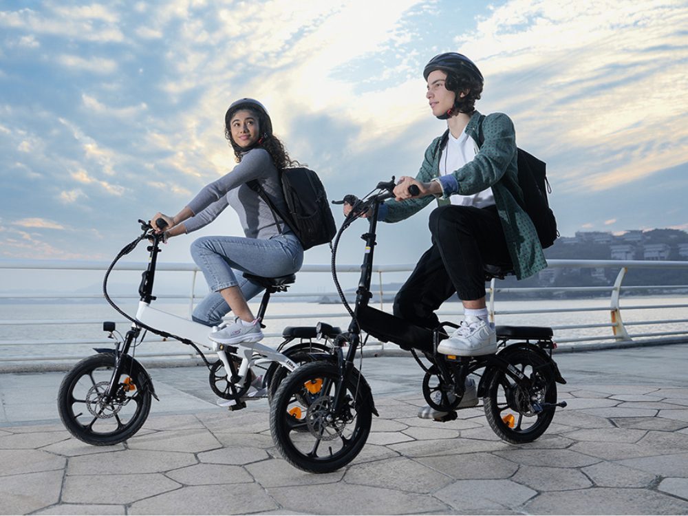 Two riders on compact folding isinwheel e-bikes on a seaside promenade